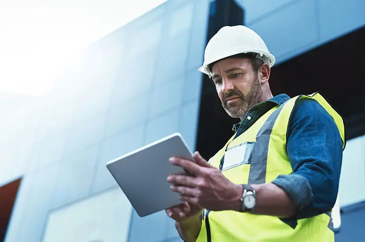 Construction worker standing in front of a building looking at tablet